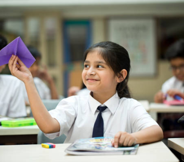 Schoolgirl playing with paper airplane in classroom